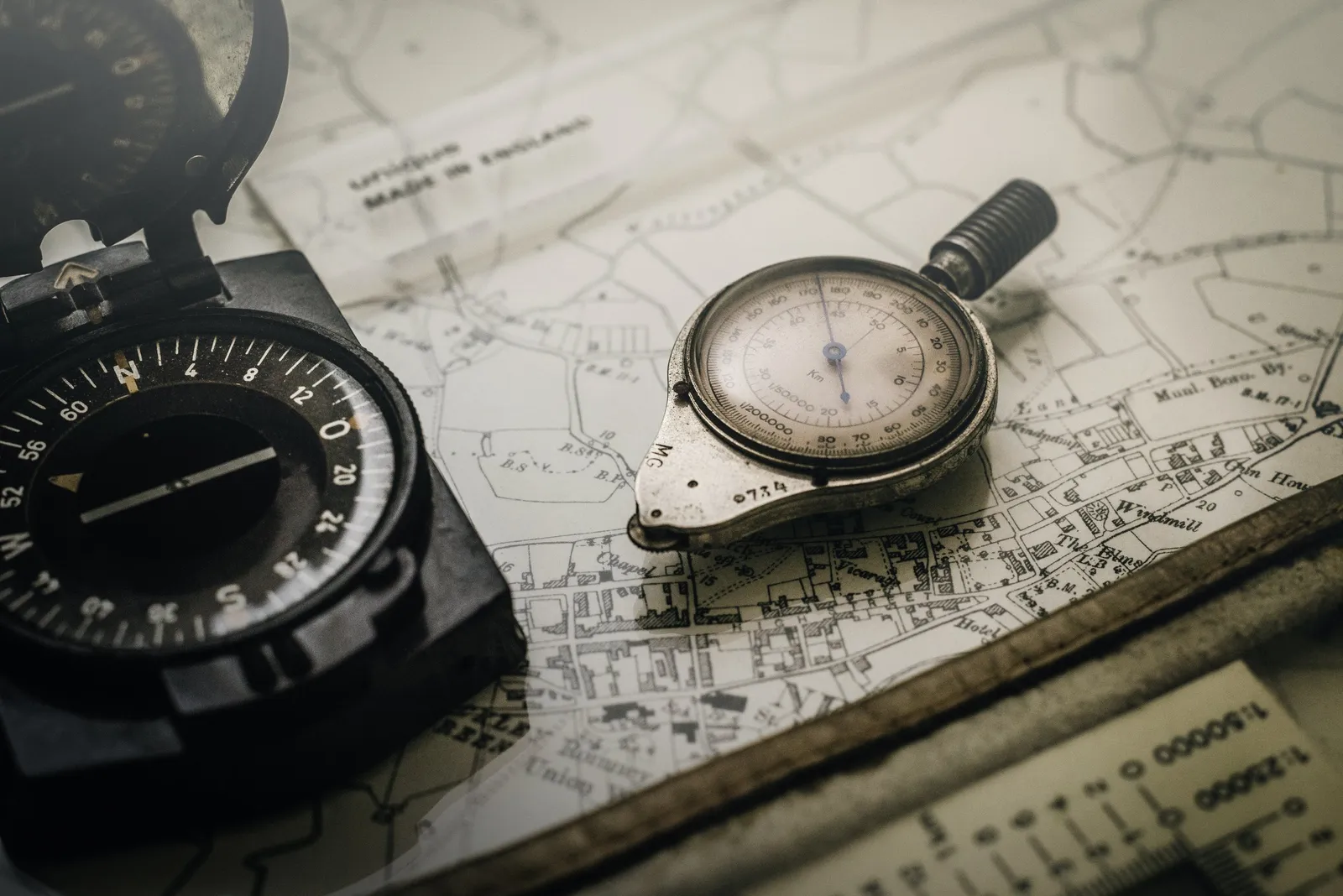 A vintage compass and a map-measuring wheel lying on an old map