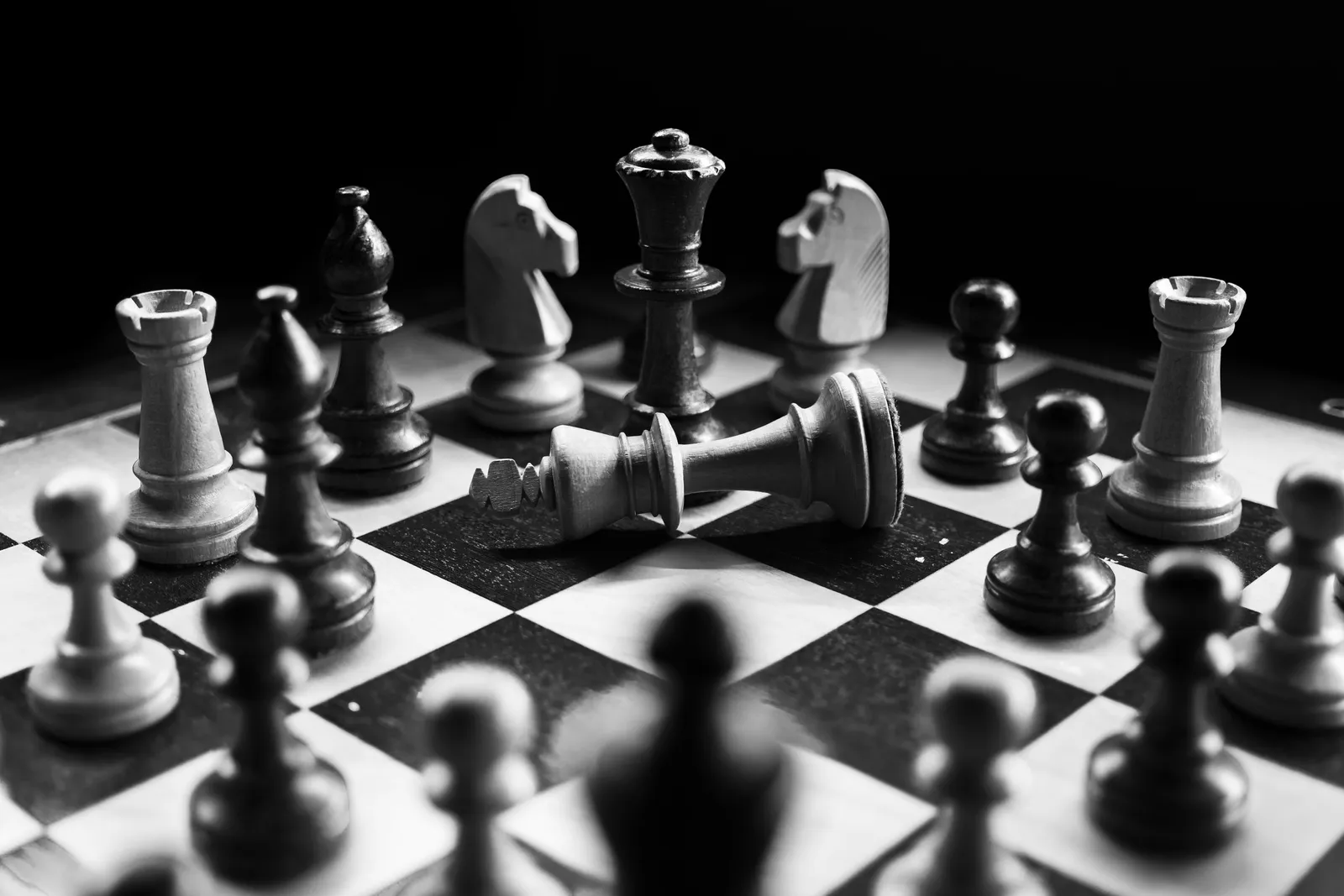 A black-and-white chess board with a fallen white king among the pieces