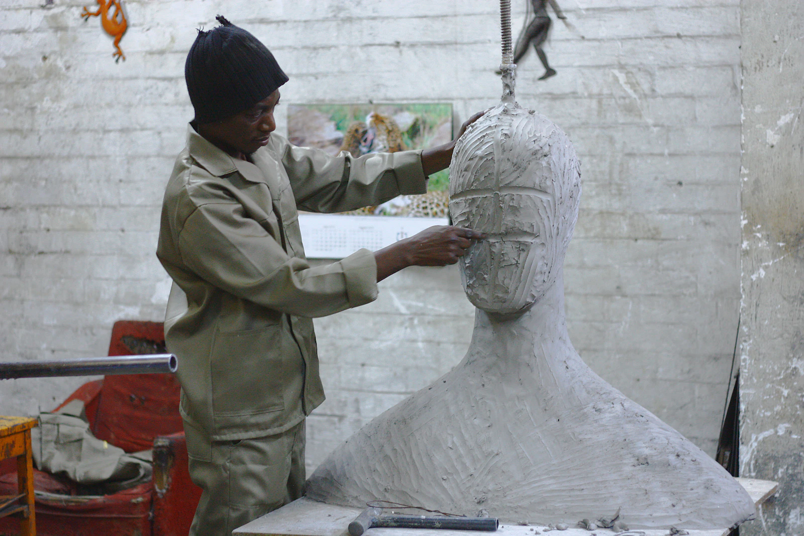 A sculptor at work in a studio, shaping a large pale figure and head